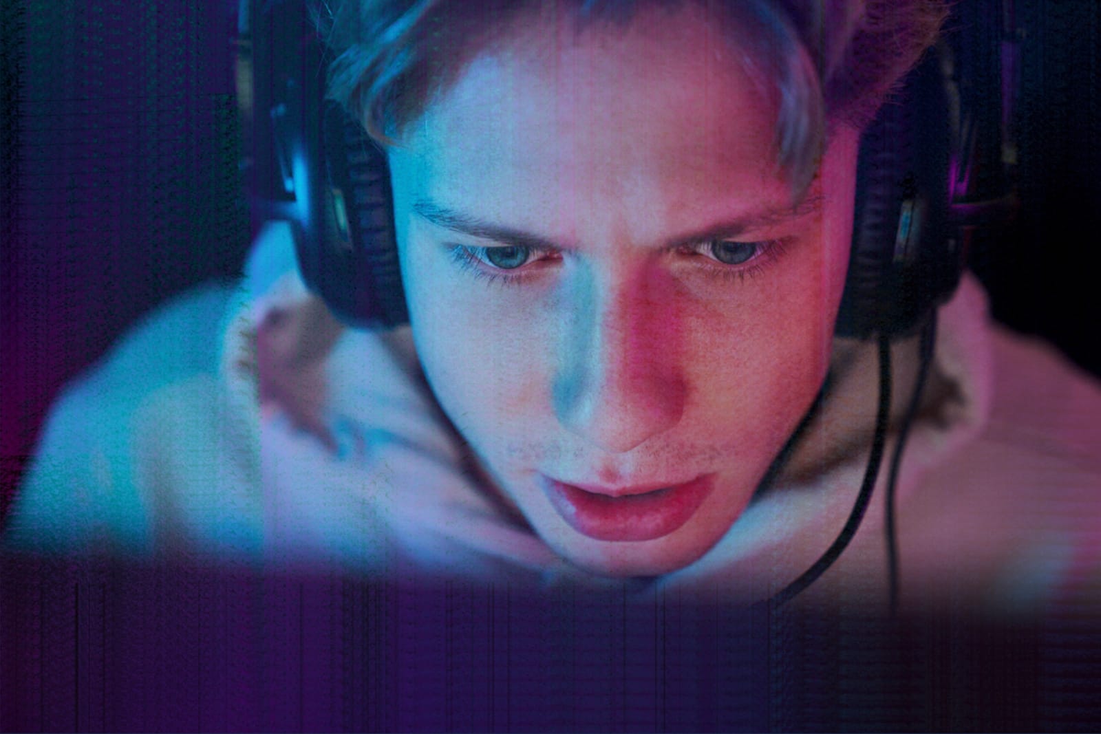 A young man wearing a gaming headset, his face lit by the glow of a screen in a dark room