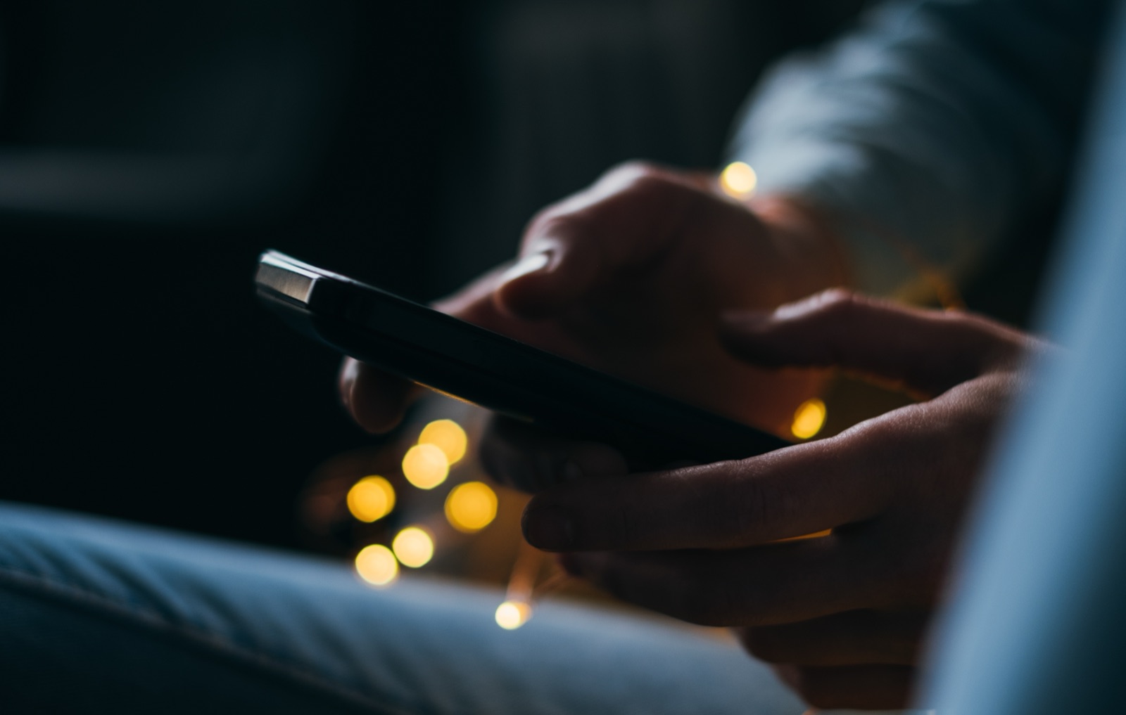 Hands holding a phone in the dark, lit by small warm lights